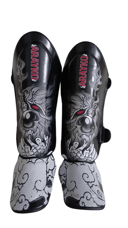 Black combat sports shin guards featuring a Thai Naga creature graphic with red eyes, ARAYKO vertical logo, and cloud-inspired foot padding