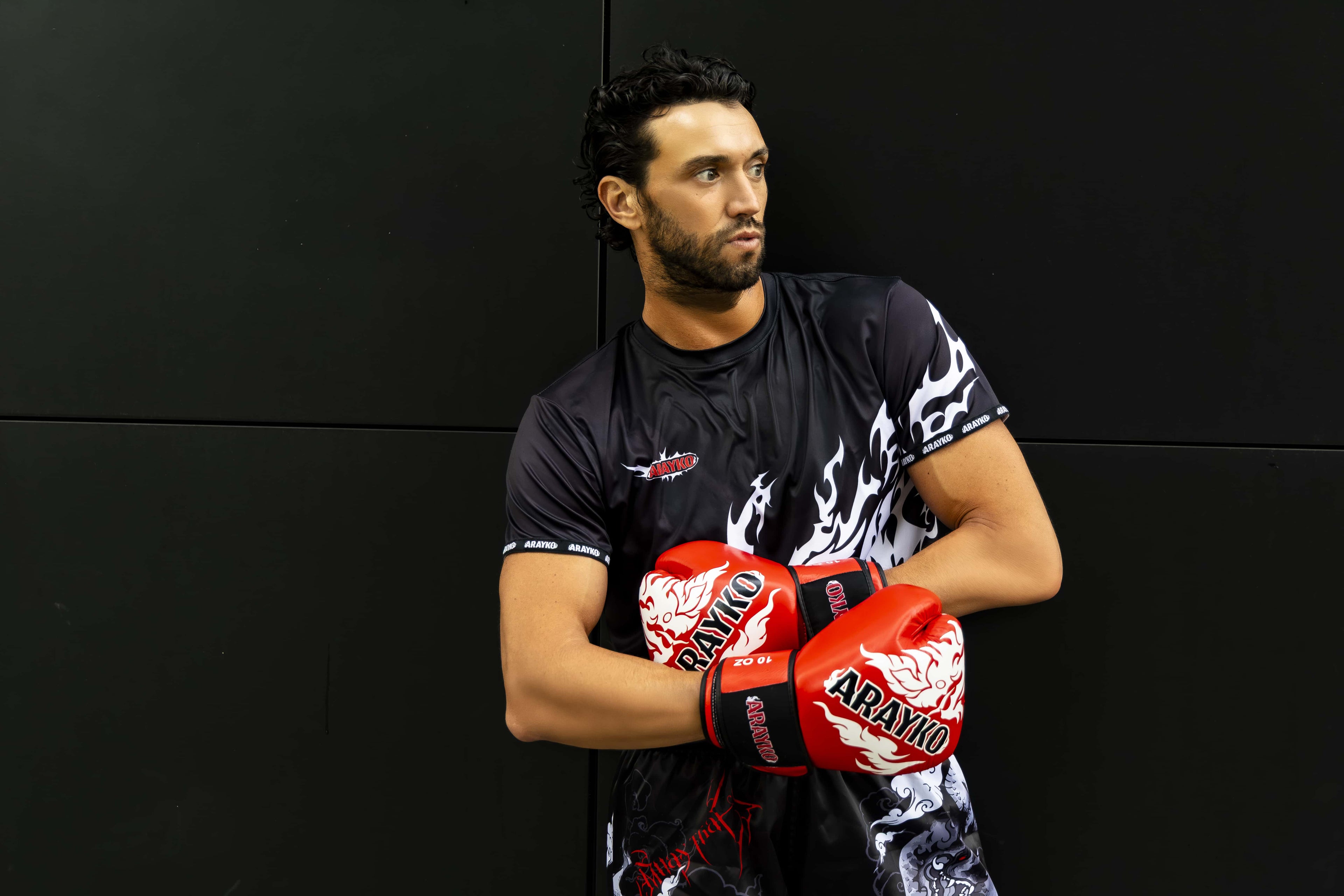 Professional athlete wearing ARAYKO boxing gloves and training apparel, posing with crossed arms against a dark background