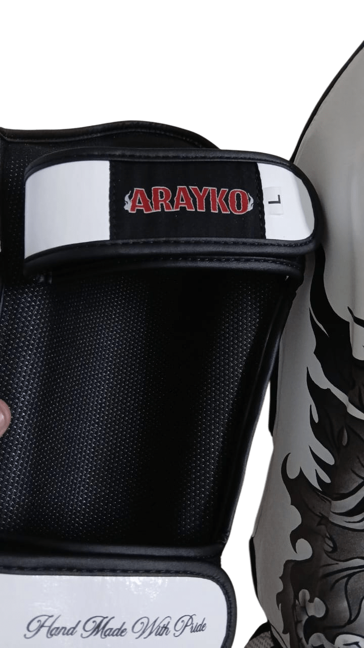 Back view of white professional shin guard showing two velcro straps: top strap with red ARAYKO embroidered logo and bottom strap with cursive 'Hand Made With Pride' text