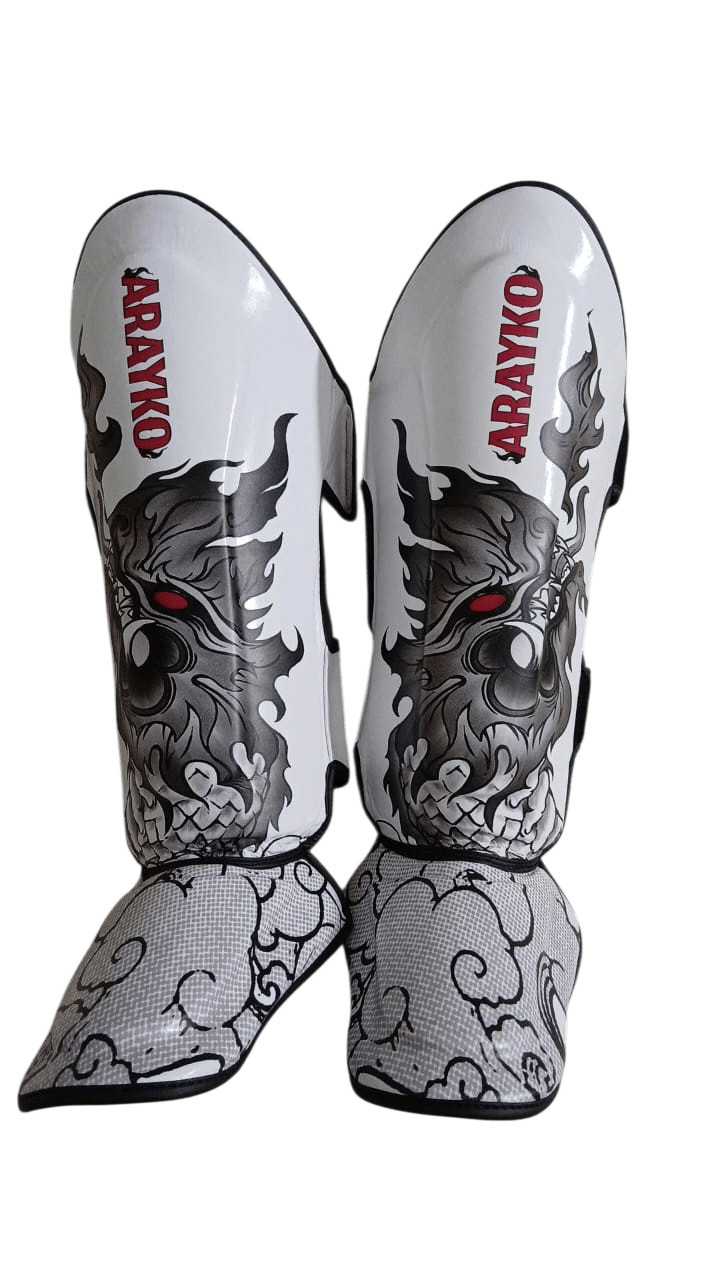 Pair of white leather shin guards with black thai dragon design and 'ARAYKO' branding on a transparent background.