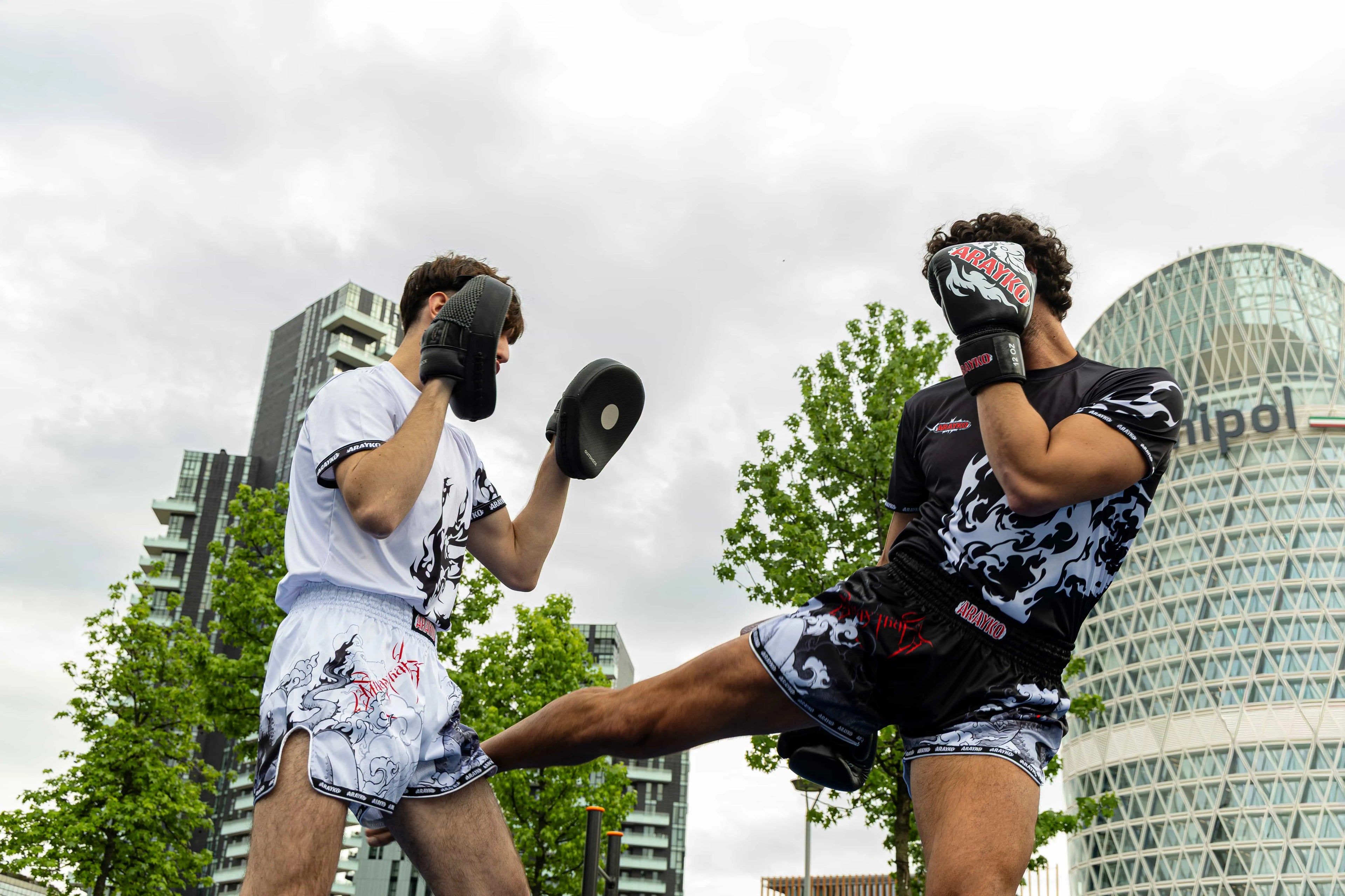 Professional kickboxer landing a low kick on a trainer wearing ARAYKO gear and apparel.