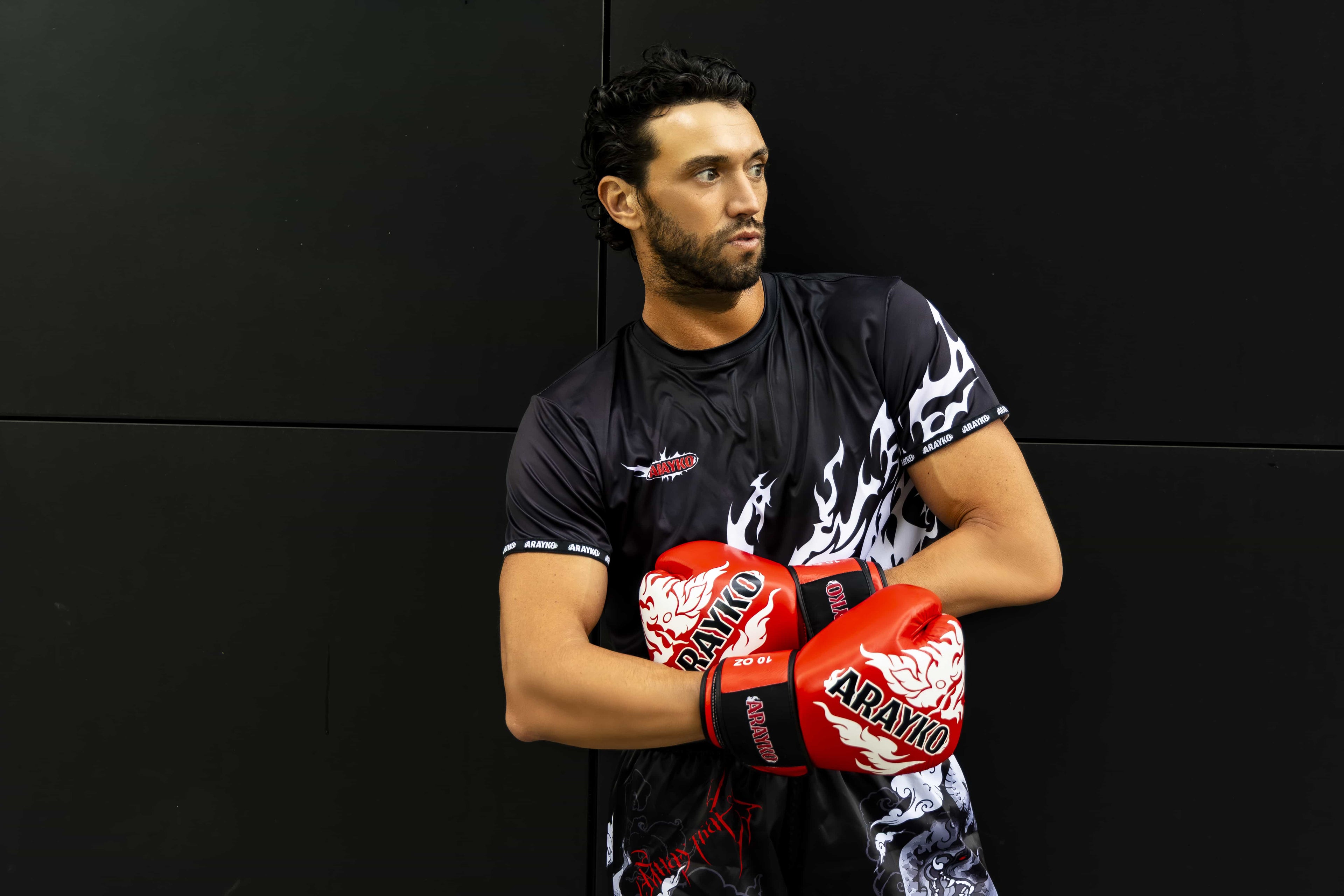 Professional athlete wearing ARAYKO boxing gloves and training apparel, posing with crossed arms against a dark background