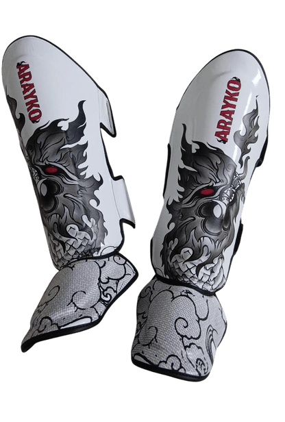 Pair of professional white Muay Thai shin guards showcasing a gray Thai dragon with red eyes, ARAYKO branding, and decorative cloud-patterned foot protection