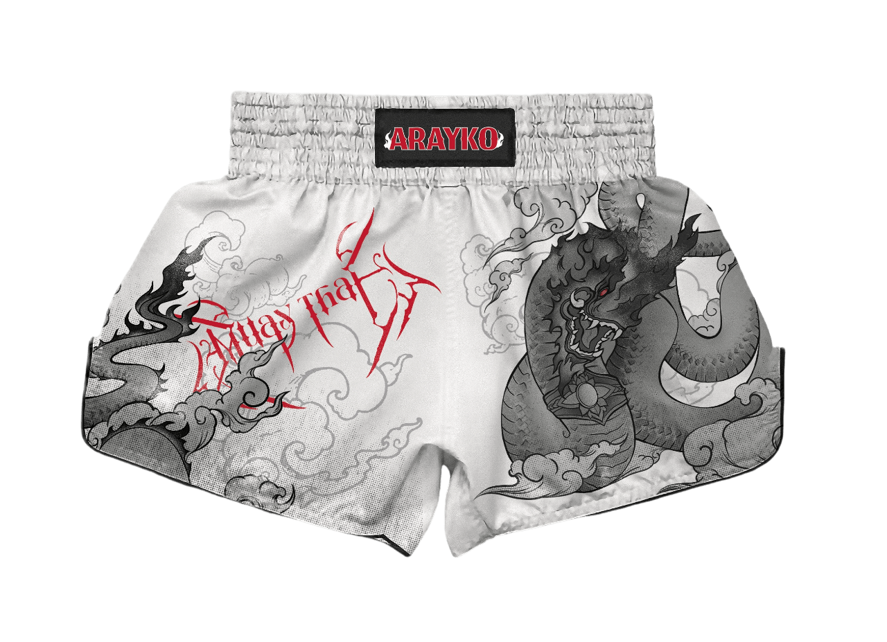 ARAYKO white Muay Thai shorts featuring a grey dragon design and red "Muay Thai" script. These professional kickboxing shorts include a traditional elastic waistband and sublimated combat sports graphics.